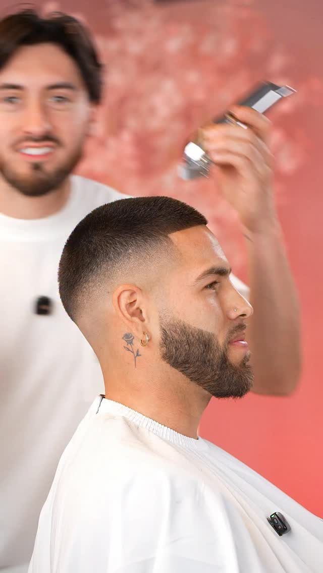 Man with a high fade haircut and beard getting a trim from a barber.