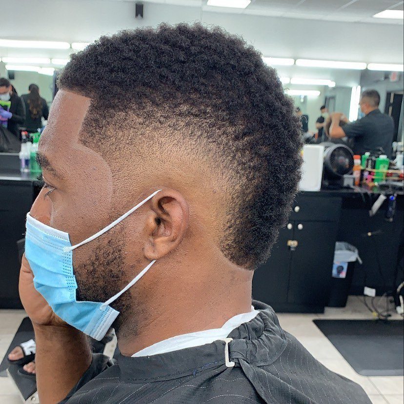 Man with a high fade mohawk haircut and curly hair in a barbershop.