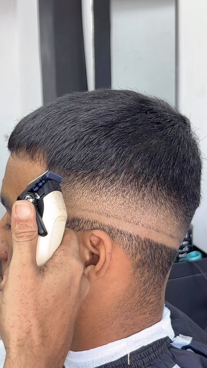 Man receiving a high fade haircut with a shaved line detail above the ear.