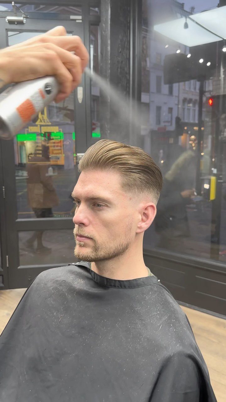 Man with a high fade slick back haircut receiving hairspray in a barbershop.