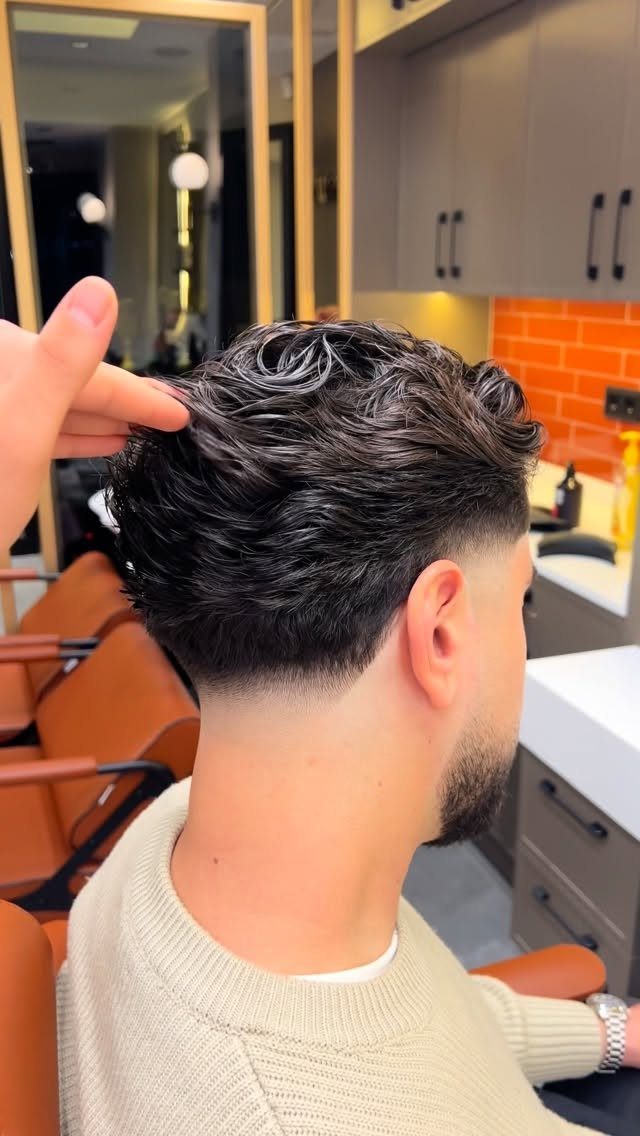 Man with dark wavy hair and a high fade haircut in a barbershop.