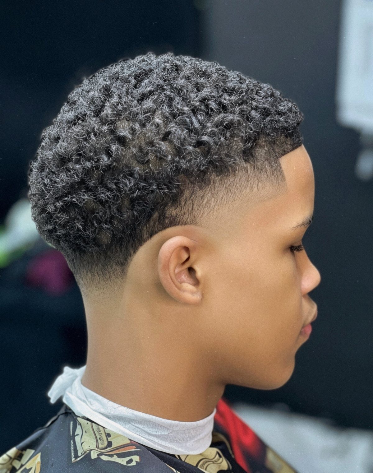 Young man with curly hair featuring a high taper fade haircut side profile