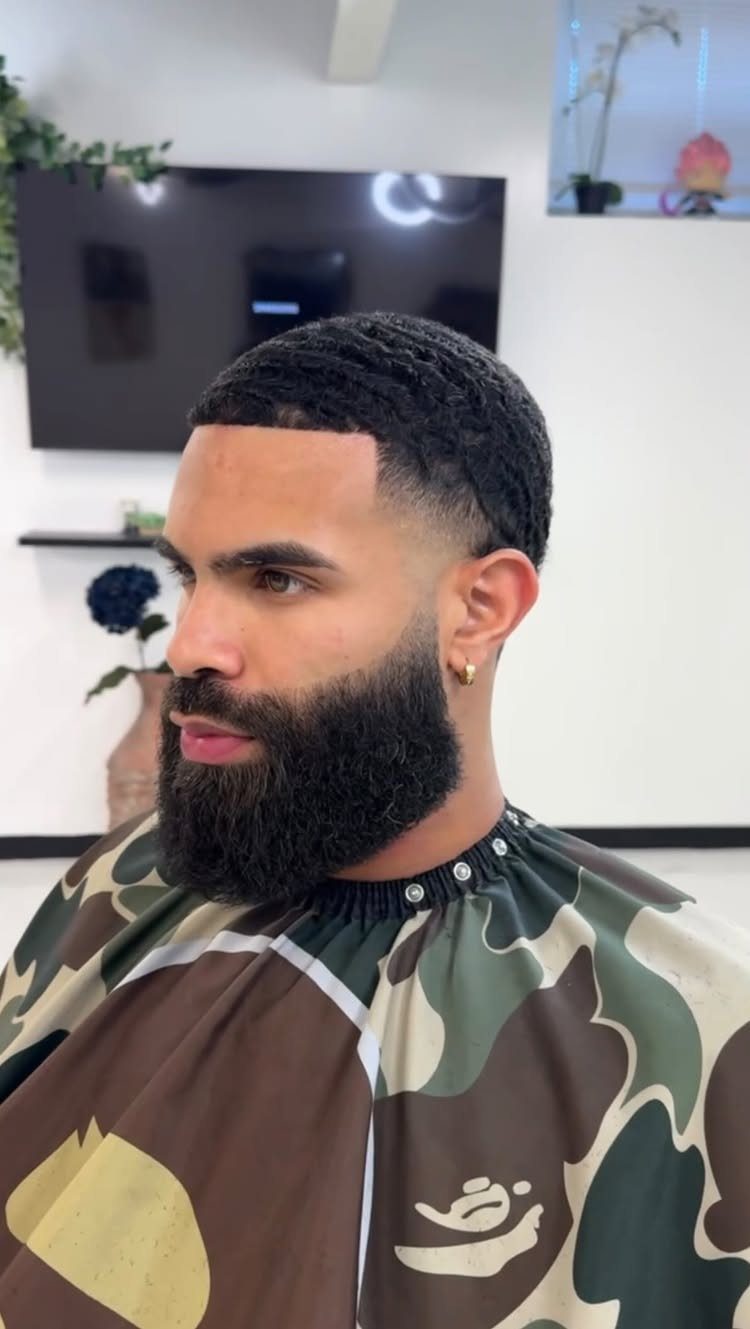 Man with a high taper fade haircut and a full, shaped black beard.