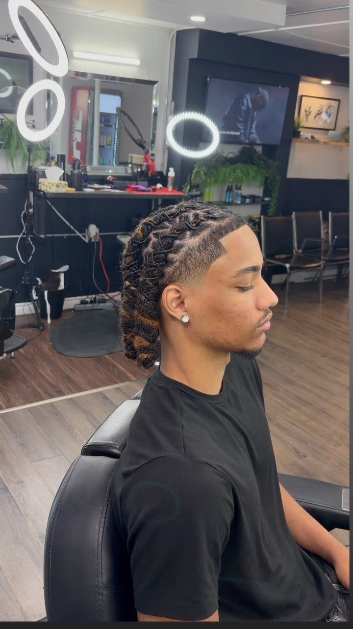 Man with long dreadlocks and a sharp high taper fade in a barbershop.