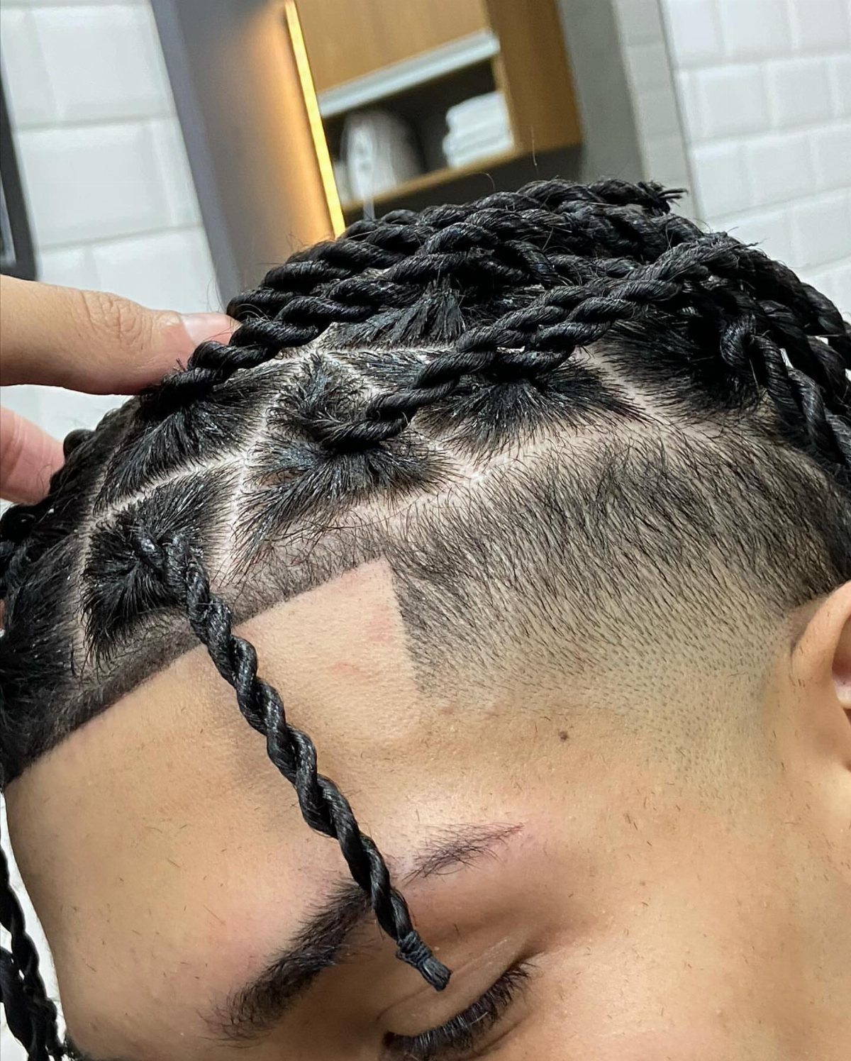 Man with black hair twists on top and a high taper fade haircut.