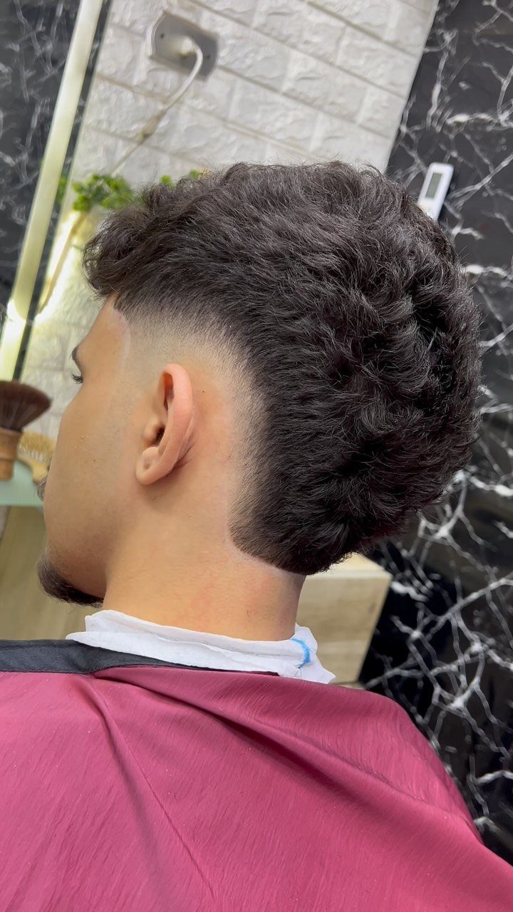 Man with a high taper fade and curly dark hair in a barbershop