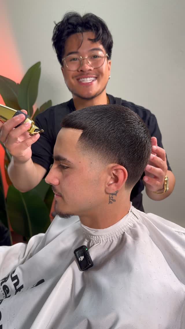 Barber finishing a short high taper fade haircut on a man in a cape
