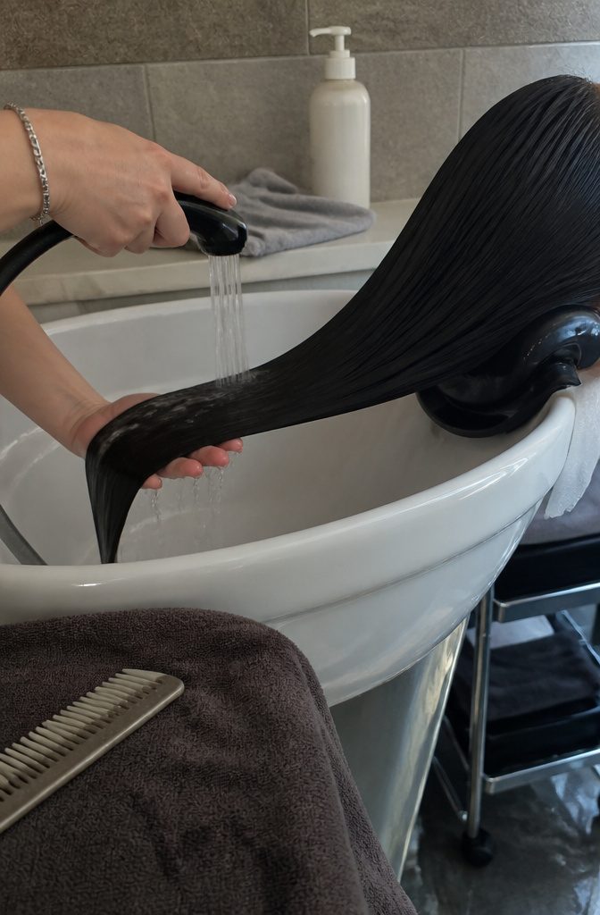 Stylist rinsing dark hair under lukewarm water in a basin