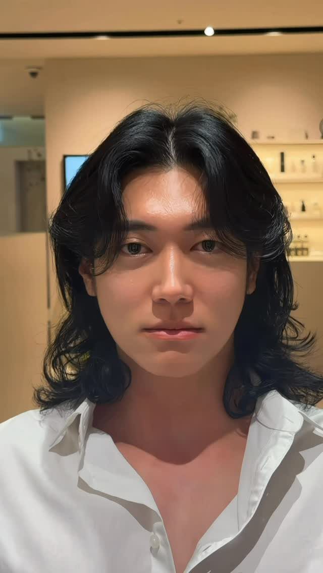 Man with long, glossy black wavy hair parted in the middle wearing white shirt