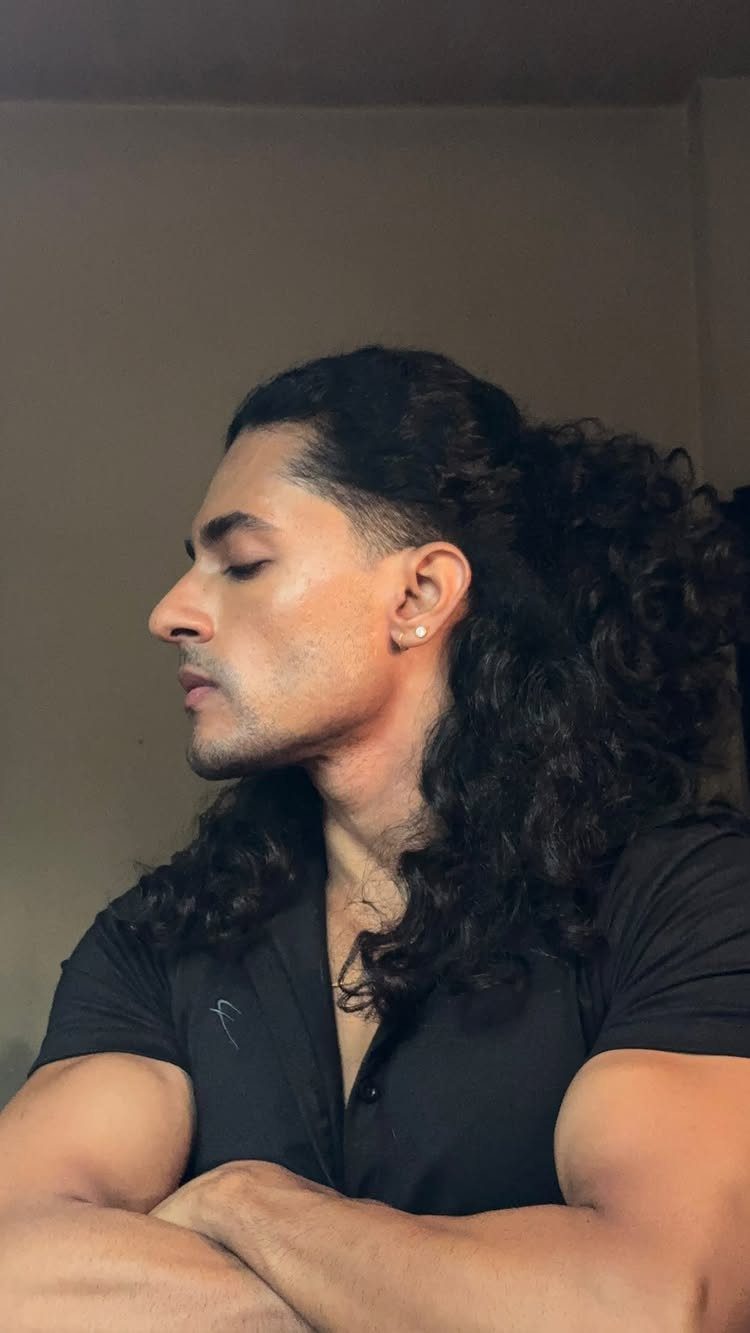 Man with long dark curly hair tied half-up, wearing a black polo shirt.