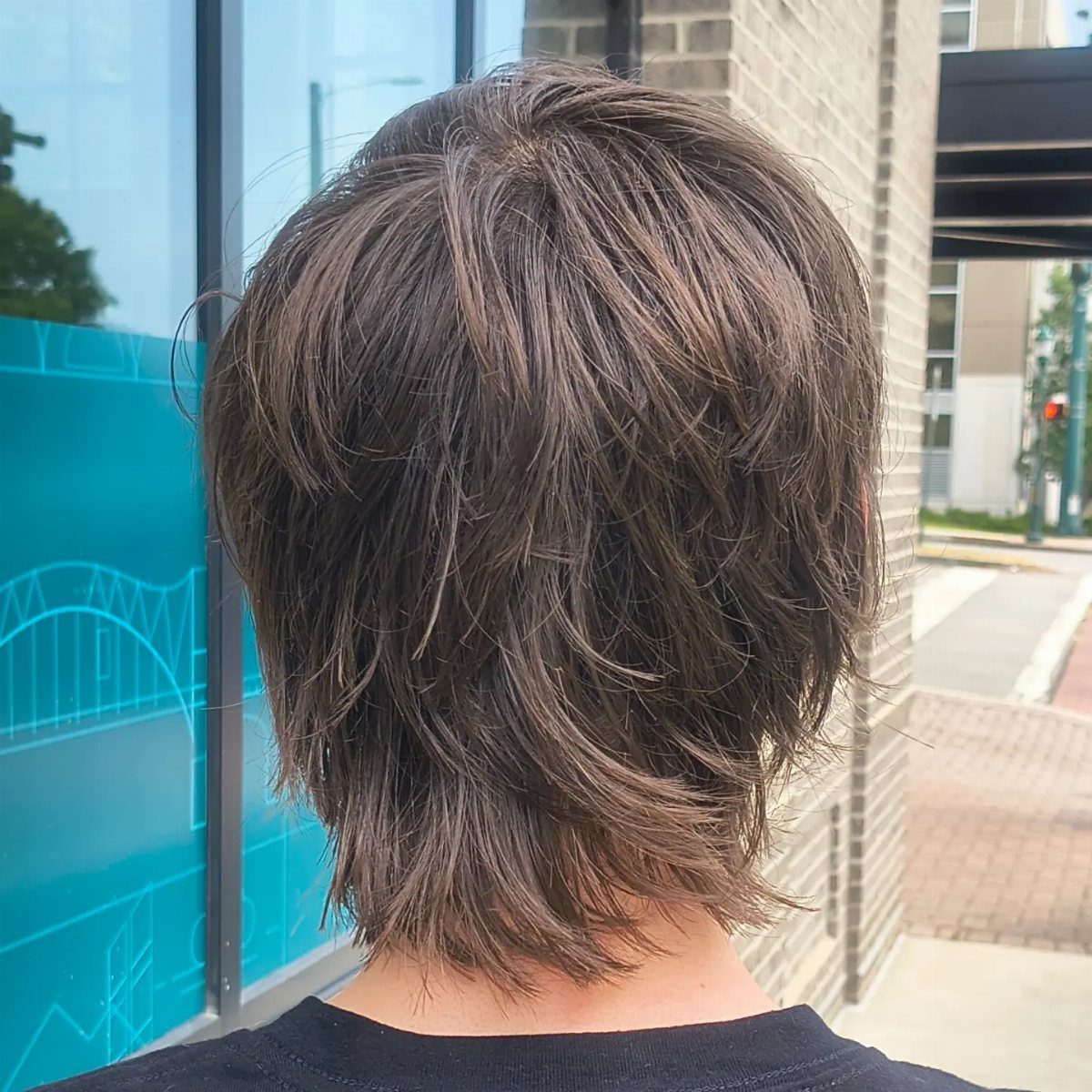 Brown layered wavy hair on a man viewed from behind outdoors.
