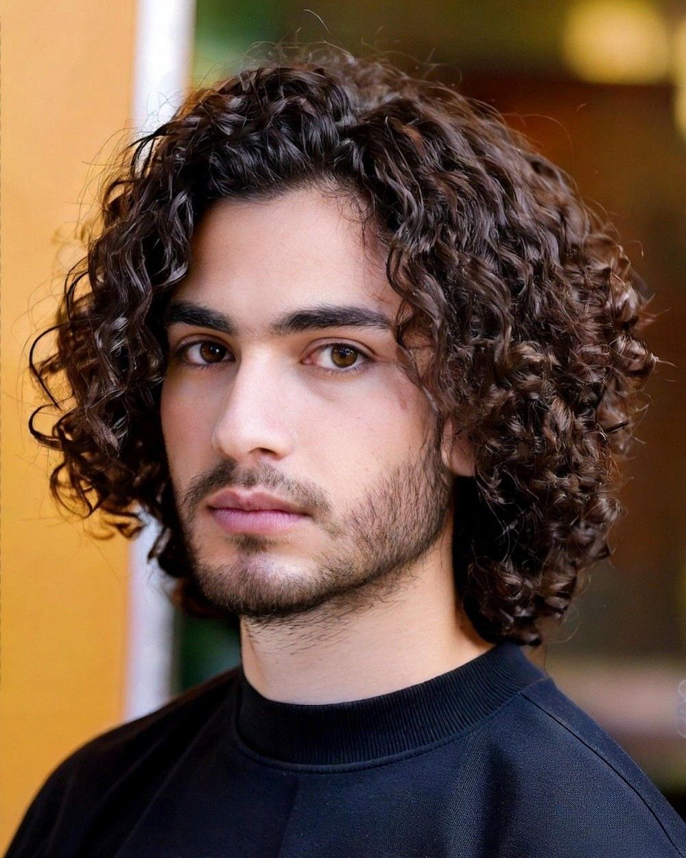 Man with long brown curly hair and a beard wearing a black shirt.