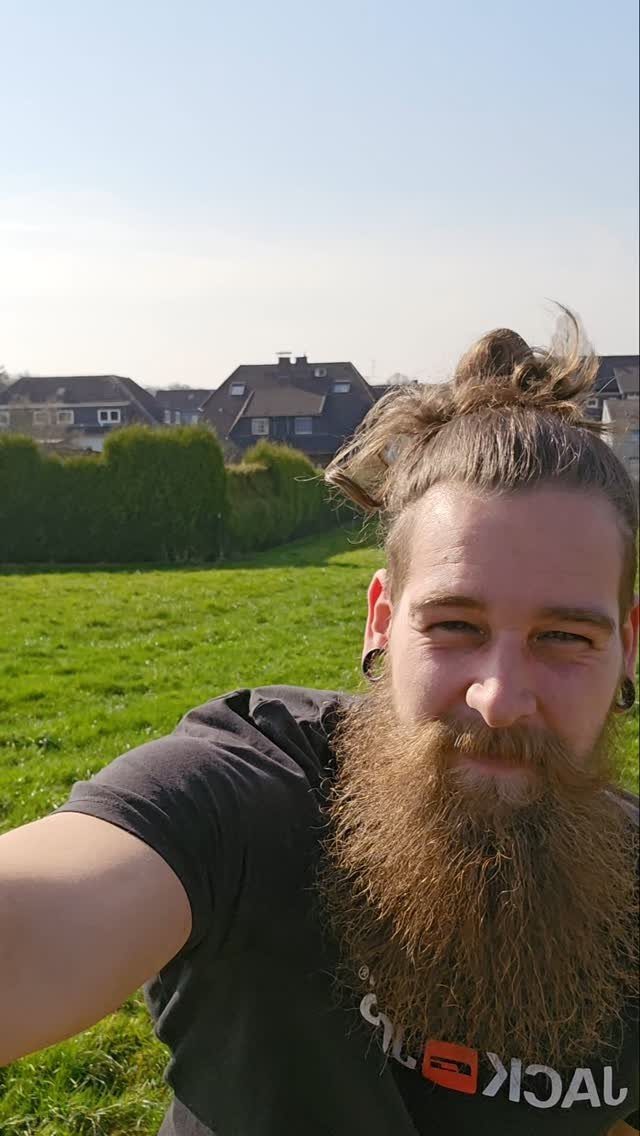 Man with a long brown beard and hair tied in a bun outdoors.