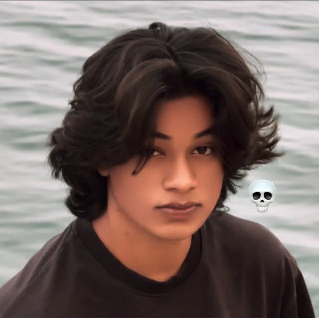 Young man with voluminous dark brown wavy hair styled with a middle part.