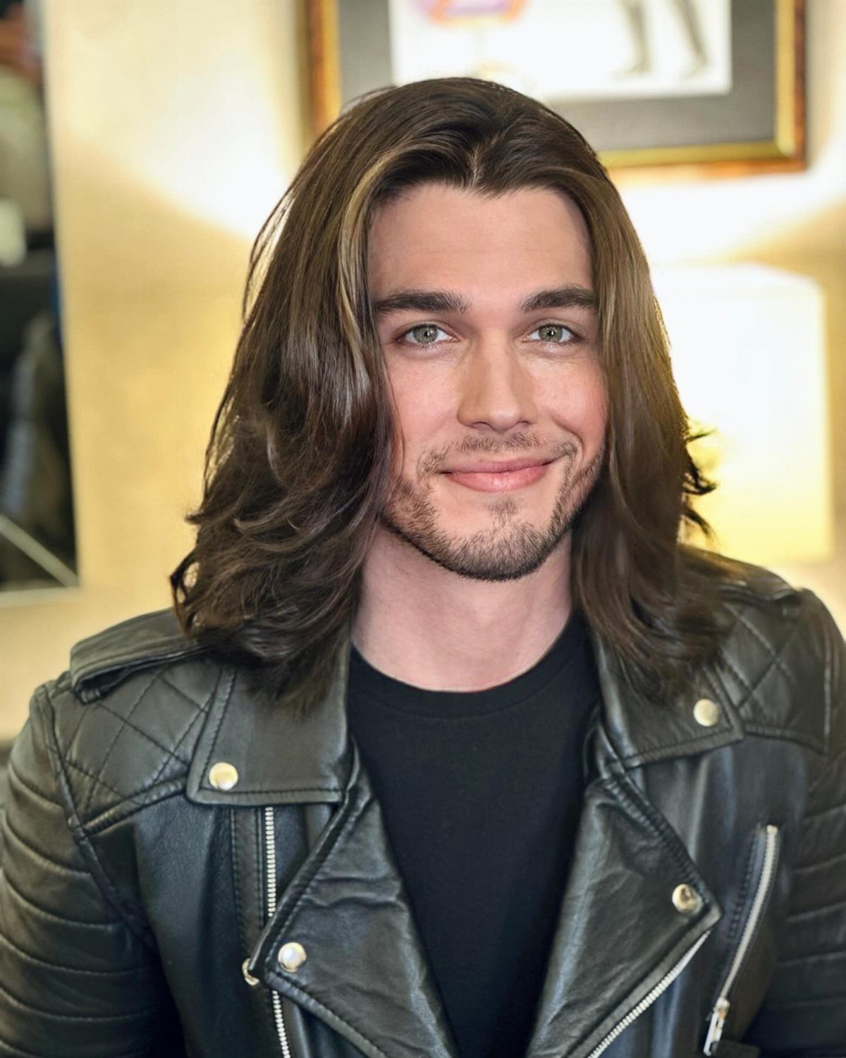Man with long brown layered hair and a beard wearing a leather jacket.