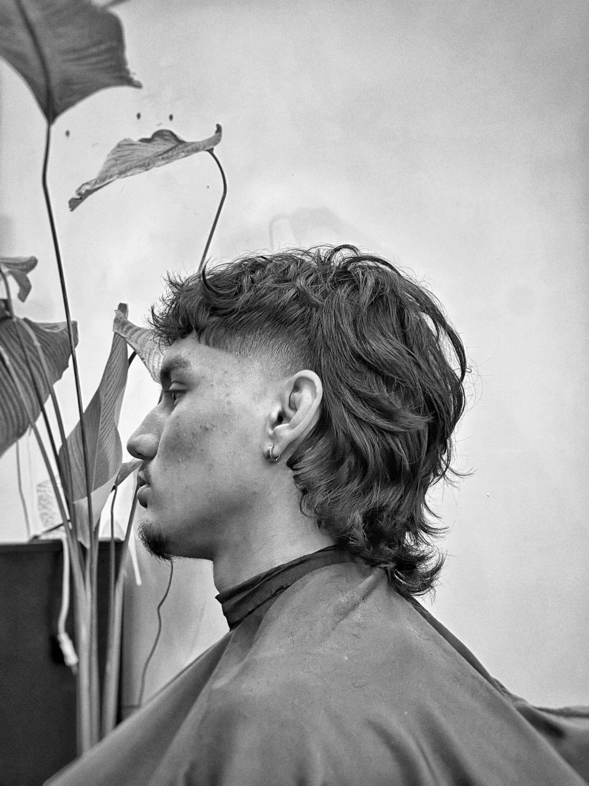 Man with a long mullet hairstyle and wavy hair in a black and white profile.