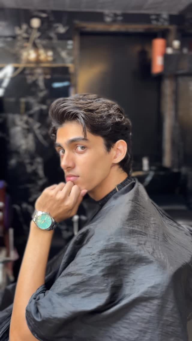 Young man with voluminous dark hair and a quiff wearing a barber cape.