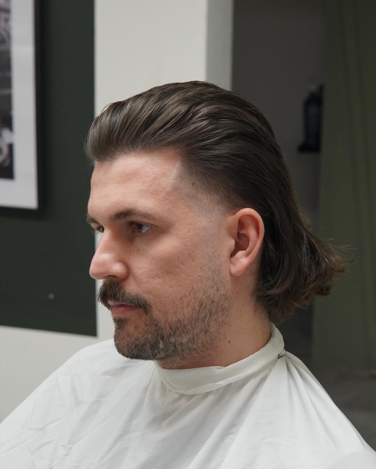Man with a slicked-back quiff and long hair in the back, wearing a cape.
