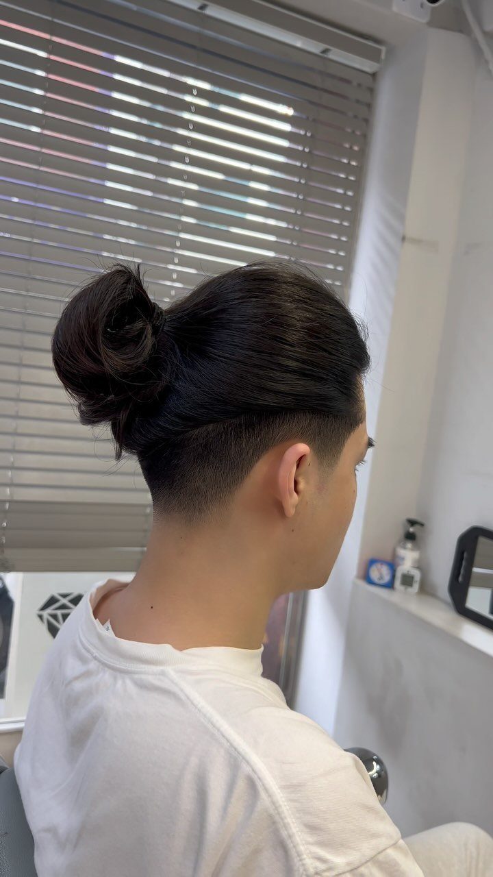 Man with dark hair in a bun and a high skin fade haircut.