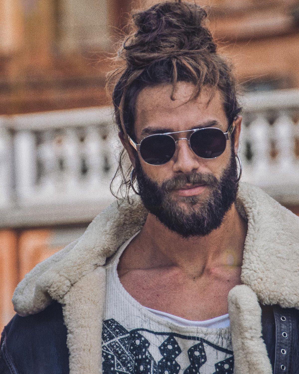 Man with a beard and sunglasses wearing his long hair in a messy bun.