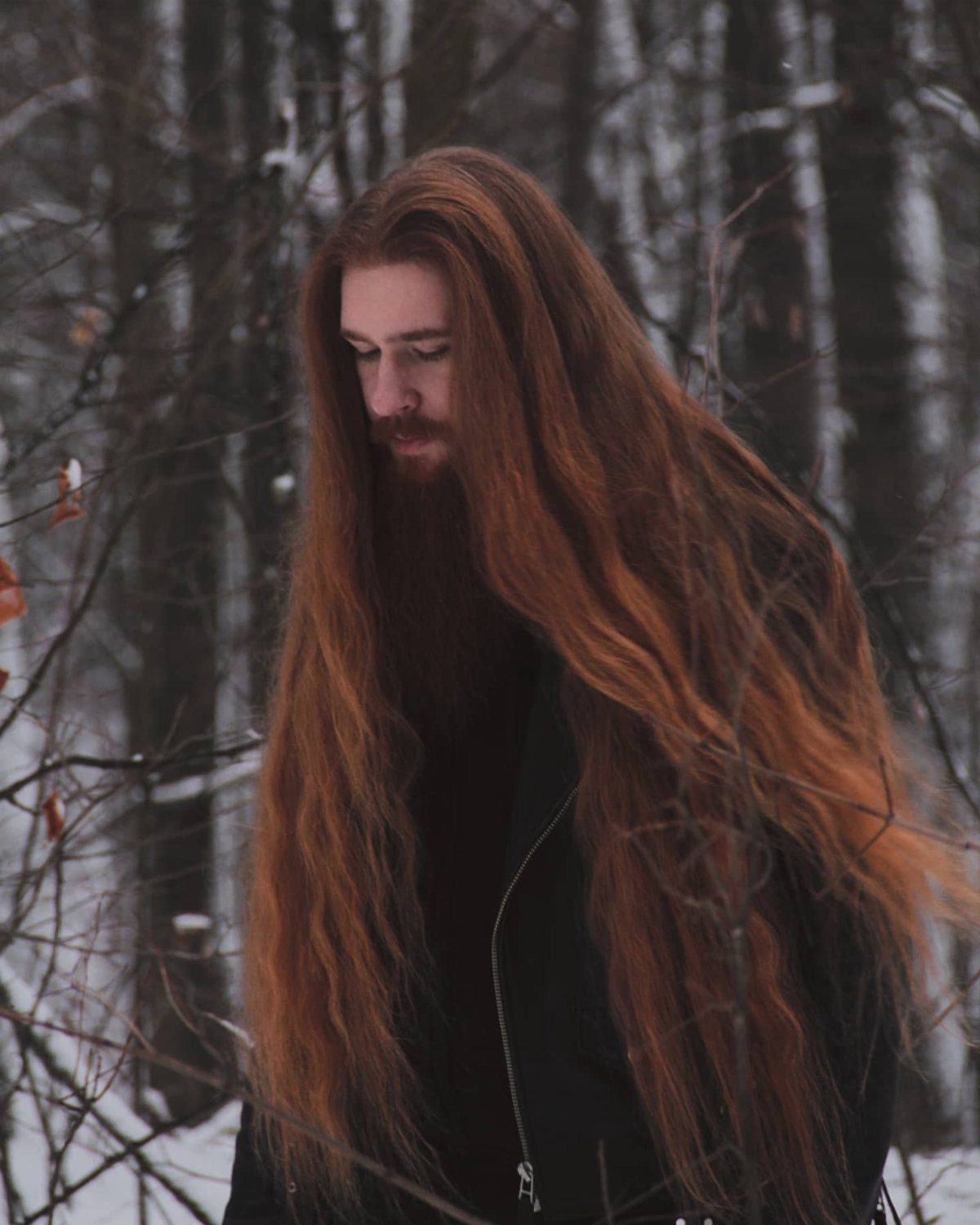 Man with very long wavy red hair and beard in a snowy forest