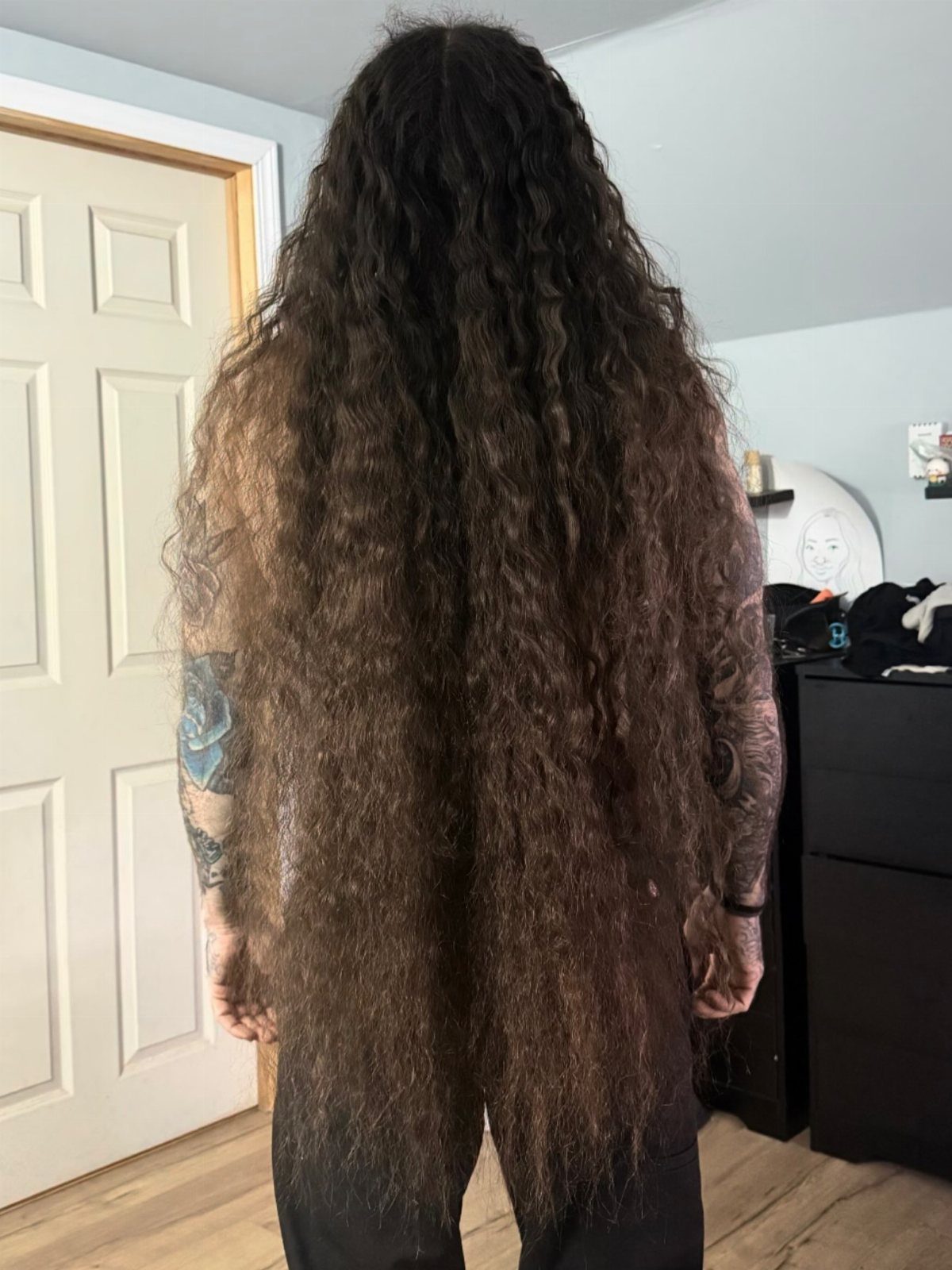 Man with very long, wavy brown hair seen from behind in a room.