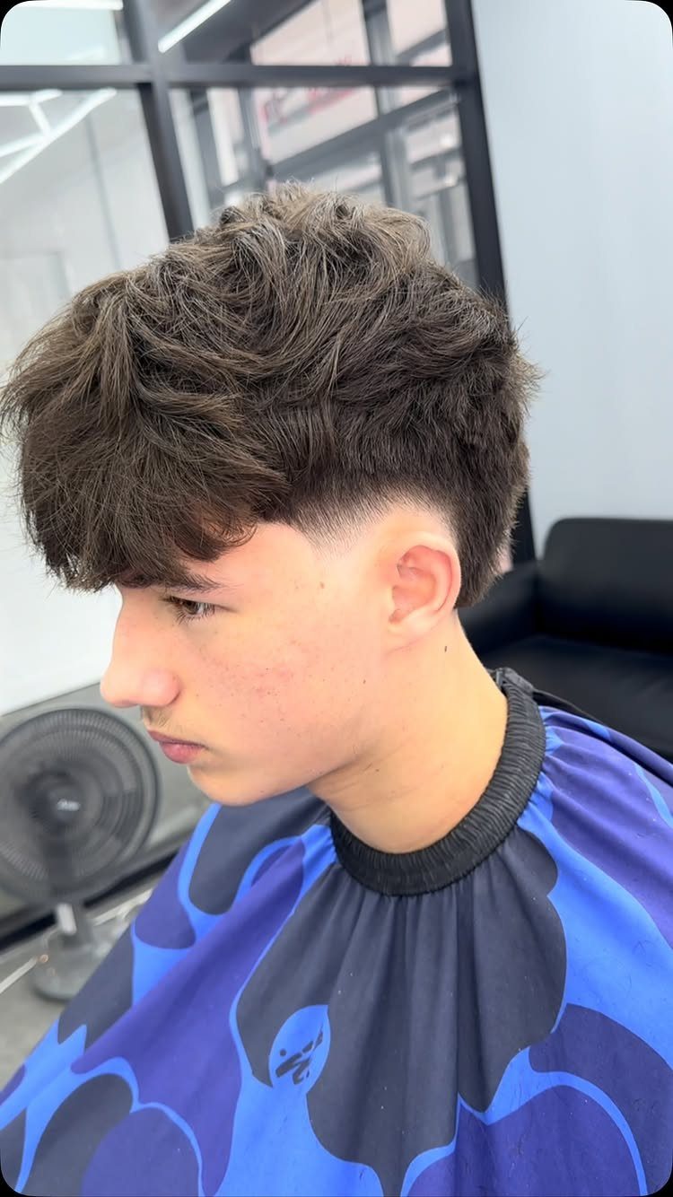 Young man with a burst fade and textured fringe covering his forehead.