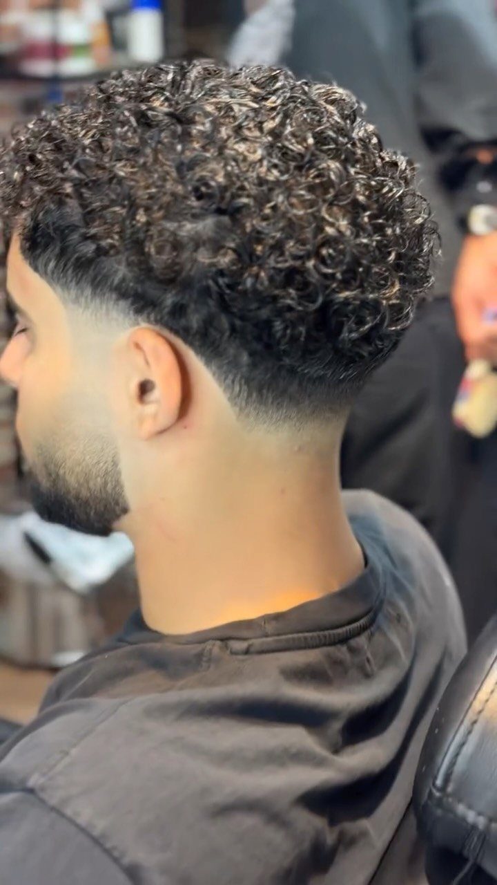 Man with tight curly hair on top and a clean low fade haircut.