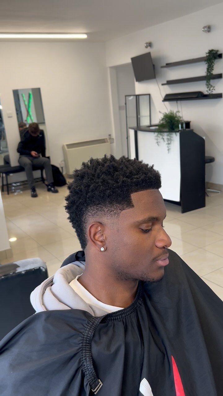 Man with a low burst fade and a textured afro top in a barbershop.
