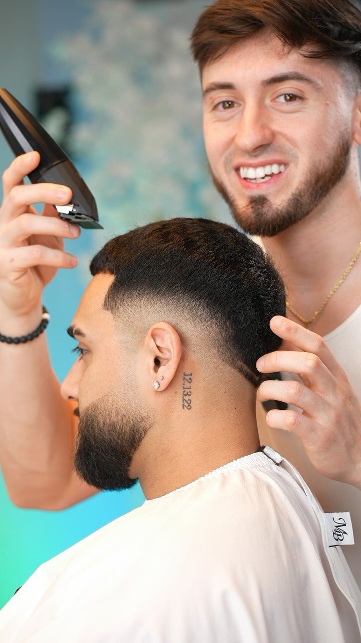 Barber trimming a man's low burst fade haircut and groomed full beard.
