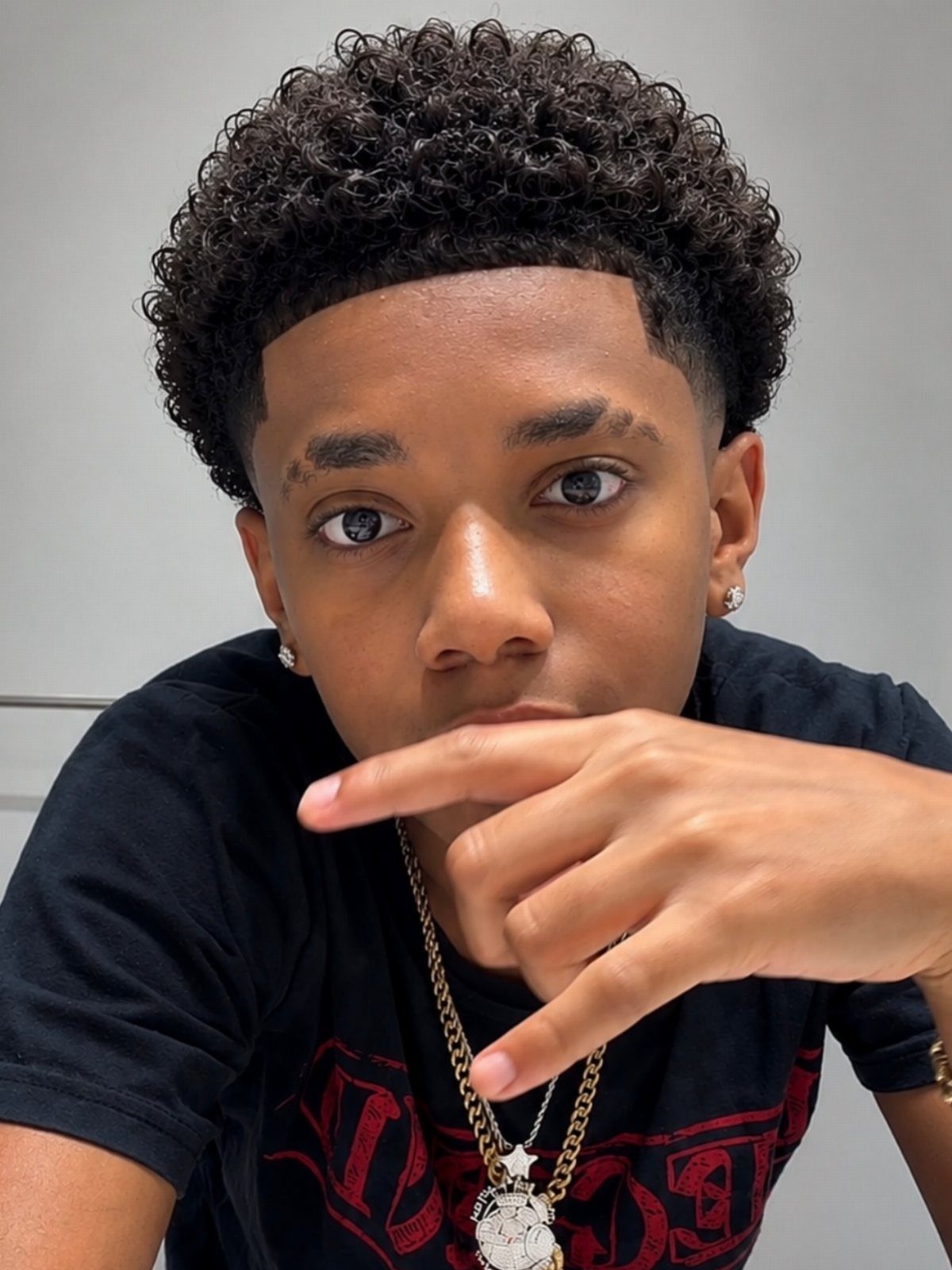 Young man with curly black hair and a low fade haircut wearing gold chains.