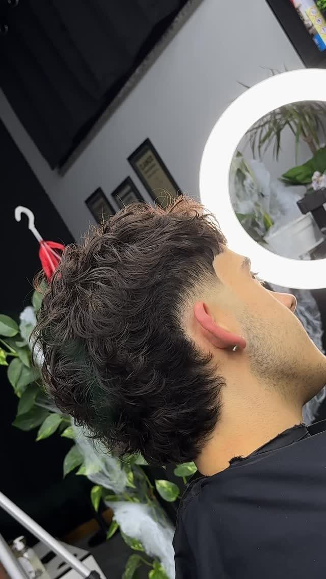Man with a low burst fade mullet and curly dark hair on top.