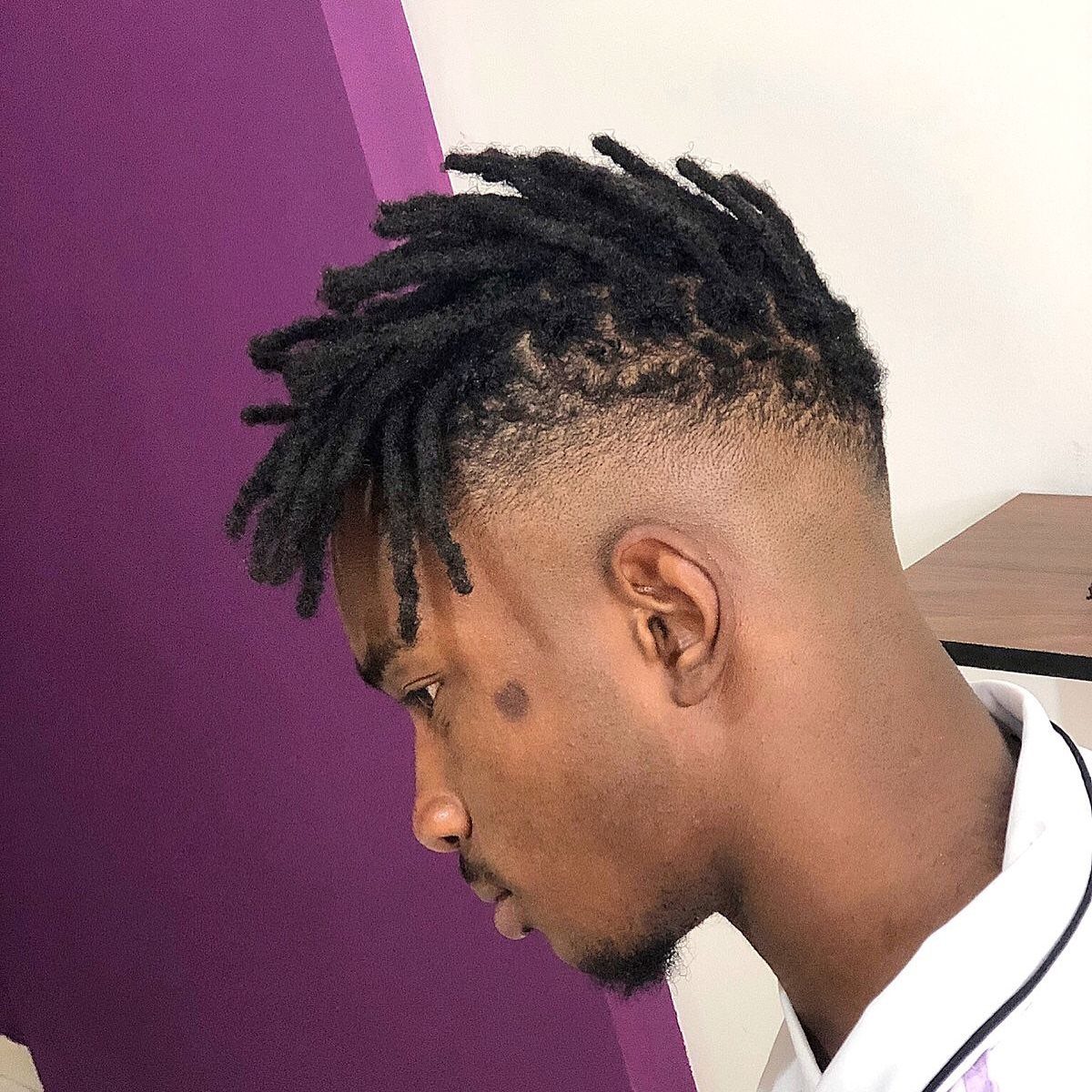 Man with short dreadlocks and a low burst fade haircut in side profile.