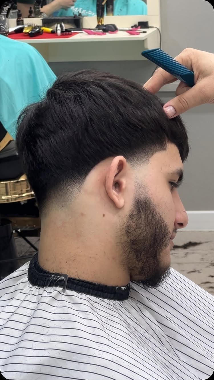 Man with a low fade haircut and full beard getting his hair combed.