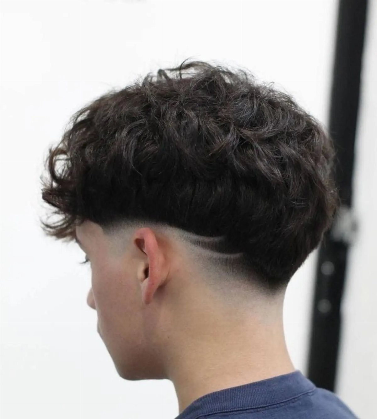 Person with curly brown hair and a low fade featuring two shaved lines.