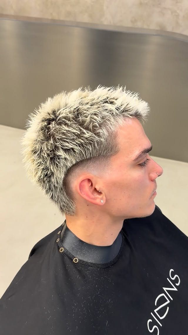 Man with a spiky blonde mohawk and a low burst fade haircut.