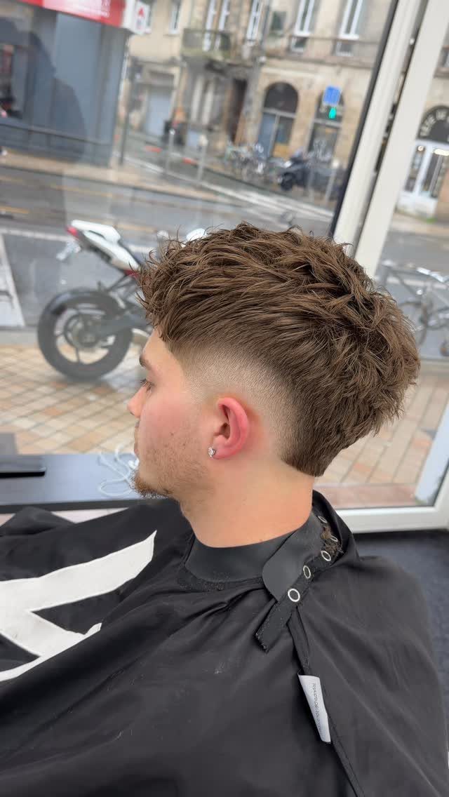 Man with a skin low burst fade and textured brown hair in a barbershop.