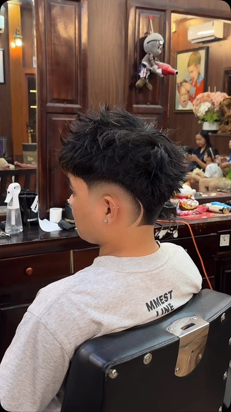 Person with a spiky mohawk and burst fade haircut in a barbershop.