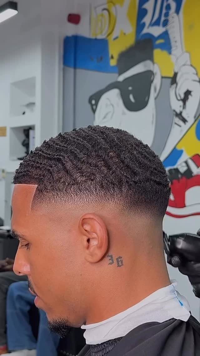 Man with a wavy low fade haircut and a neck tattoo in a barbershop.