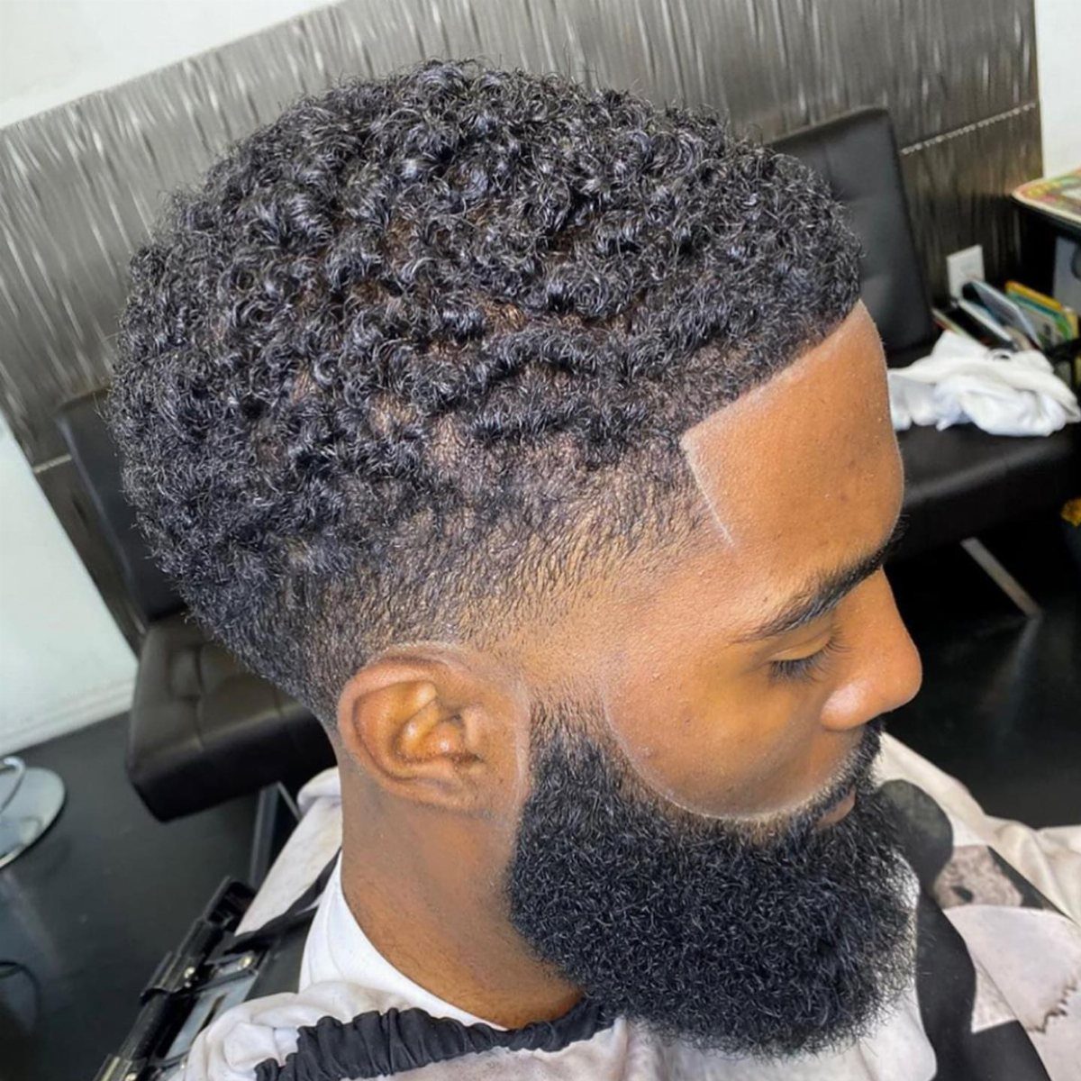 Man with curly hair, a low taper fade, and a sharp lined beard.