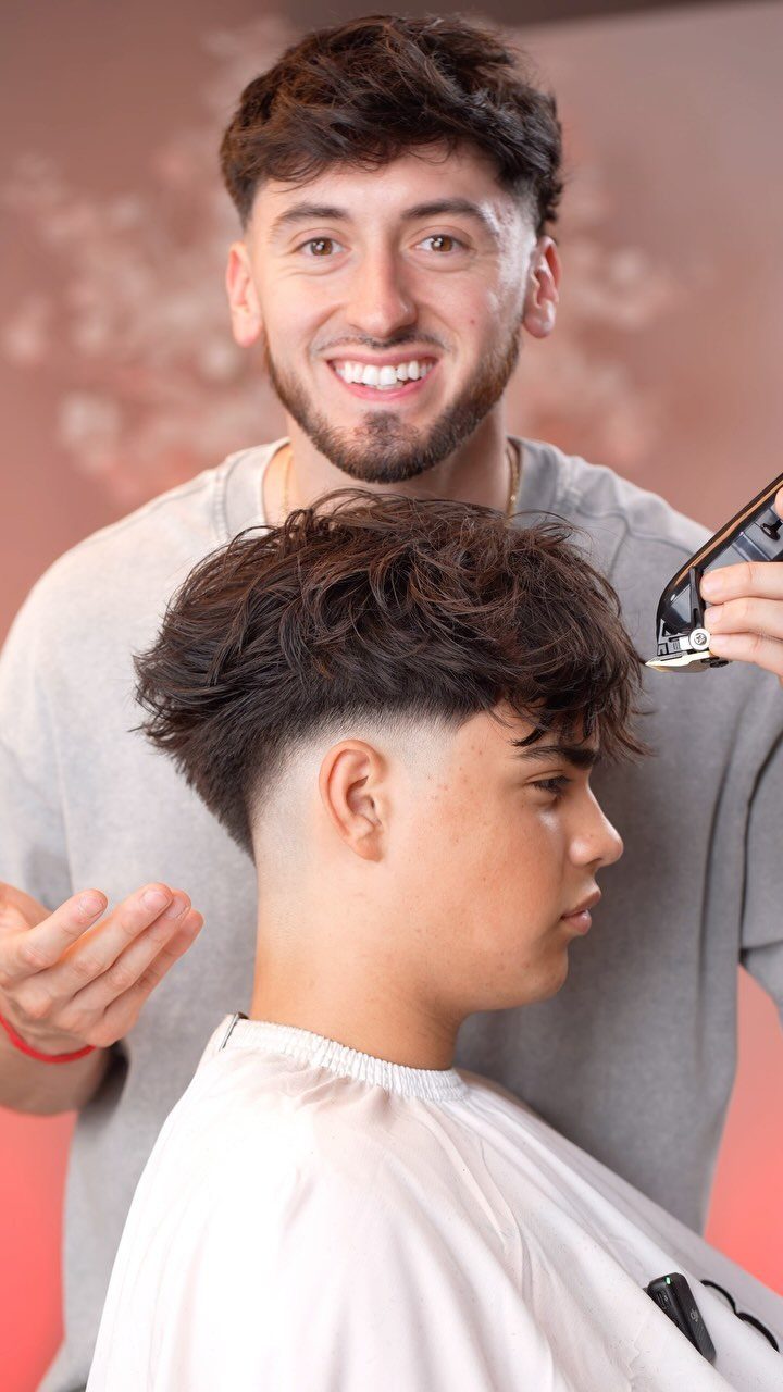 Young man with a drop fade haircut and textured top being groomed by a barber.
