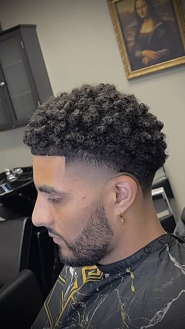 Man with curly hair and a low taper fade haircut and groomed beard.