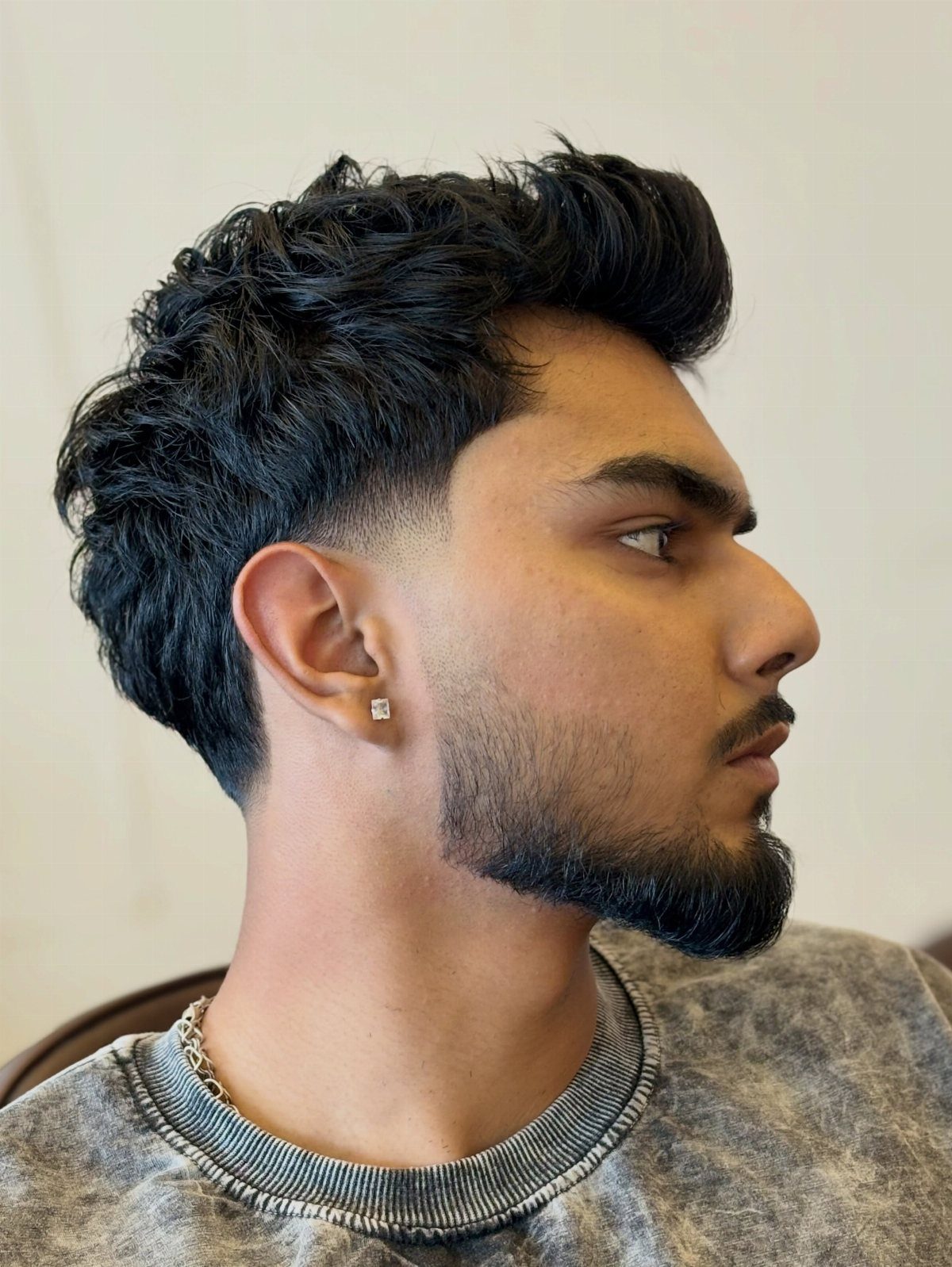 Man with a low fade haircut, wavy dark hair on top and groomed beard.