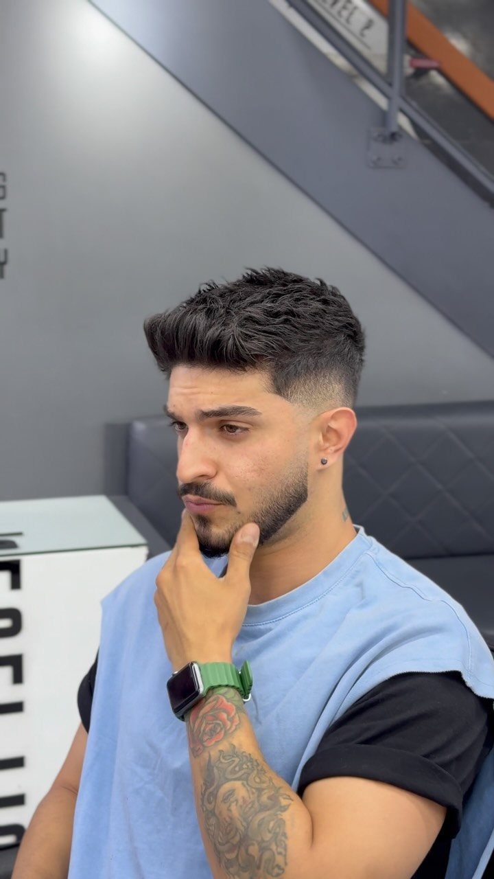 Man with a low skin fade haircut and groomed beard posing in a studio.