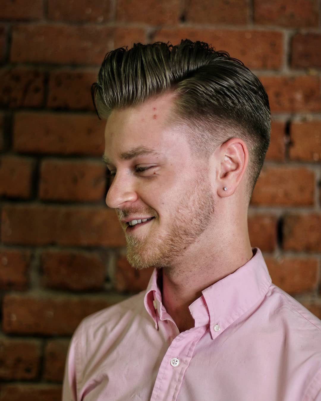 Man with a pompadour hairstyle and low fade against a brick wall