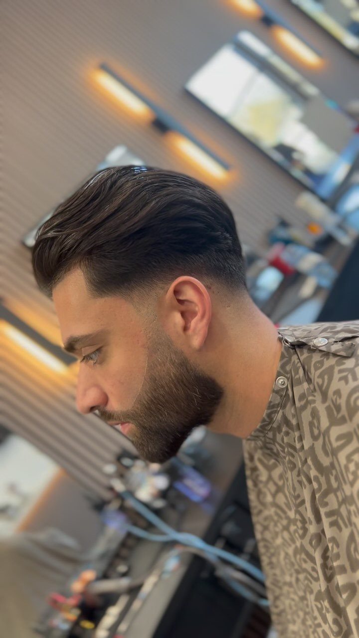 Man with slicked-back hair, low fade haircut, and a groomed dark beard.