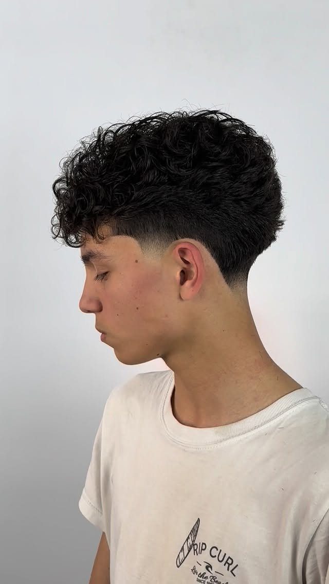 Young man with curly hair on top and a low taper fade haircut.