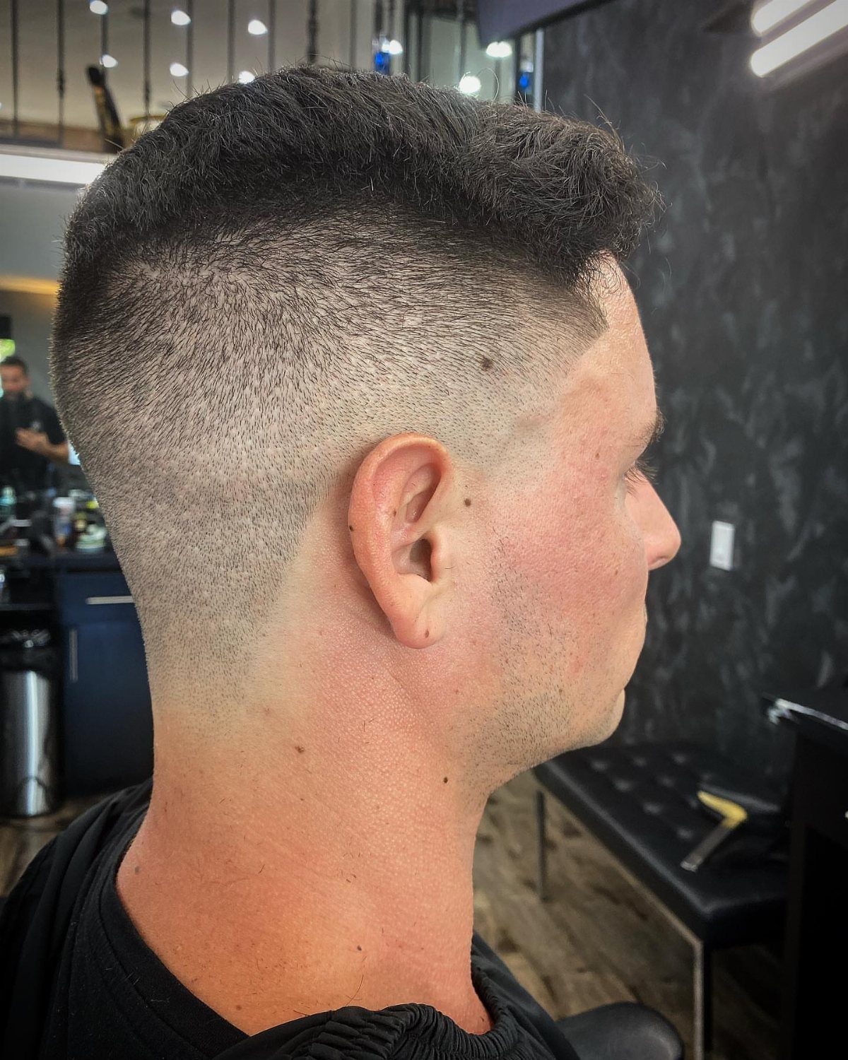 Man with a high skin fade haircut and textured short top in a barbershop.