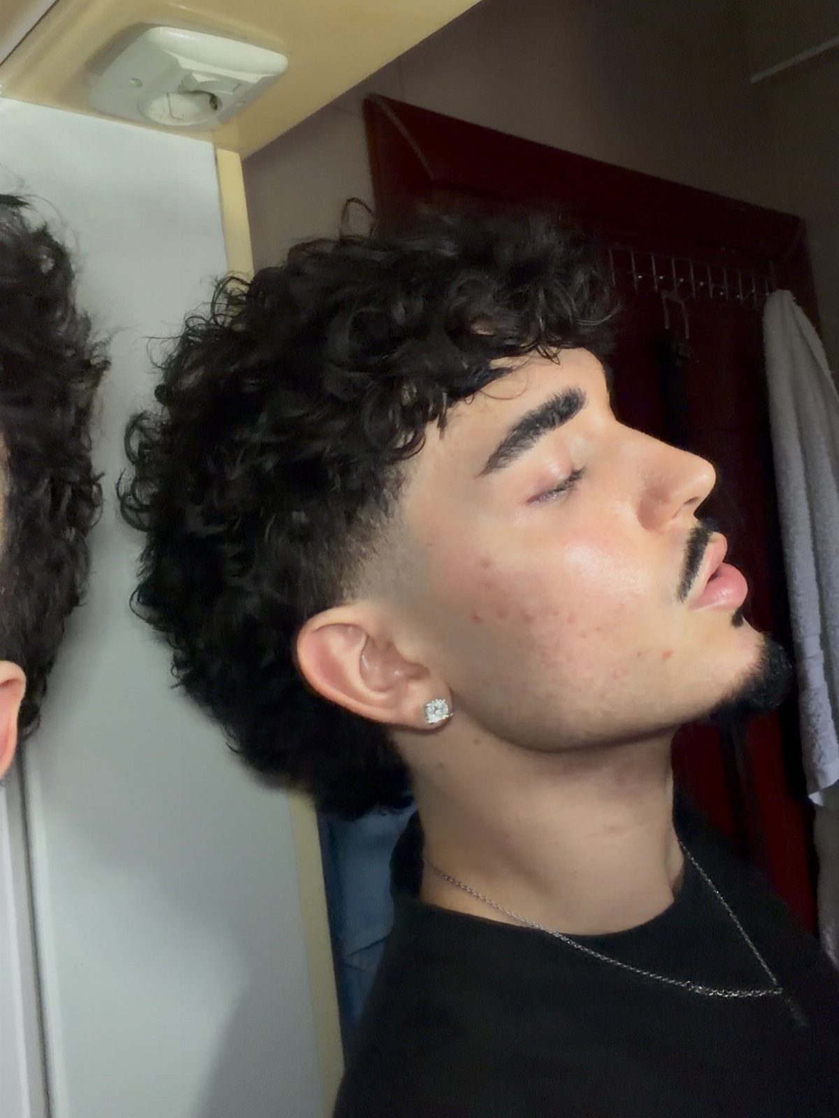 Young man with a curly mullet haircut and tapered sides in profile view.