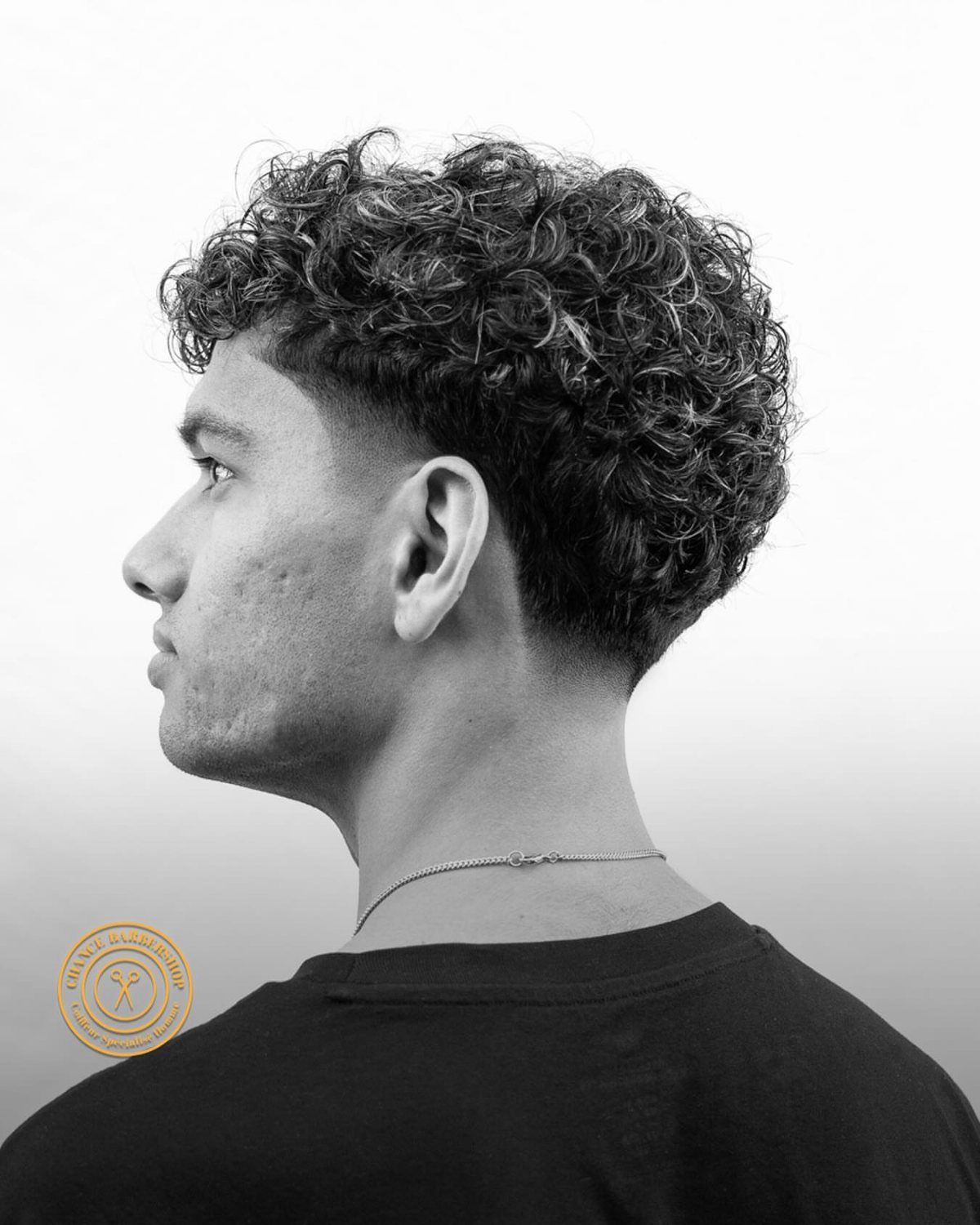 Man with curly hair on top and a low taper fade haircut profile